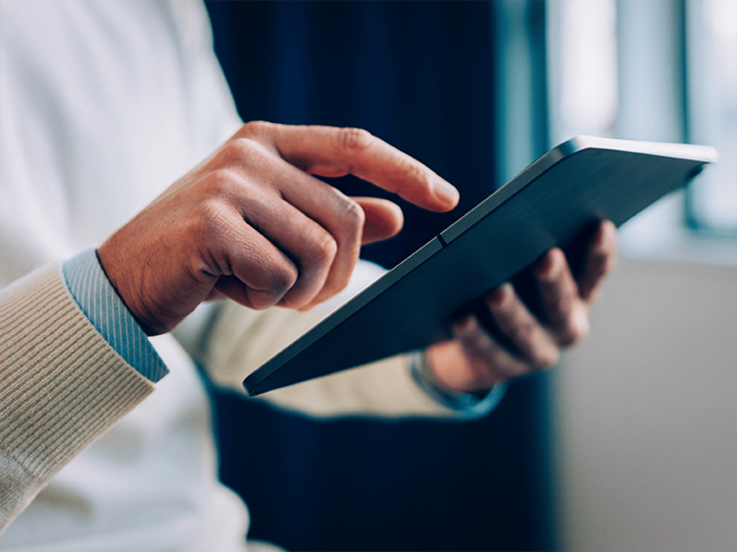 Image pictures a hand holding a tablet in one hand while scrolling on it with the other